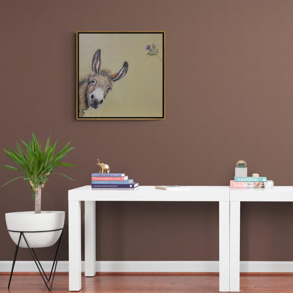 "You Called?" painted by renowned UK wildlife artist Ann Richmond, is a whimsical portrait featuring a donkey that's leaning into the painting, as if just noticing us. Or has it noticed that thistle? The piece comes alive with vibrant brush strokes over a richly textured canvas, capturing the delicate interplay of nature in a moment of quiet wonder. Each piece in The Wylde Ones is rendered in Richmond’s fresh, energetic, and gestural new style—a deliberate departure from her works in The Otherwurlde Collection. The backgrounds are carefully matched to hues from a heritage palette we affectionately call “Barrow & Fall”; complementing these striking and distinctive portrayals of British wildlife. Discover the original works and fine-art prints at Otherwurlde.com.